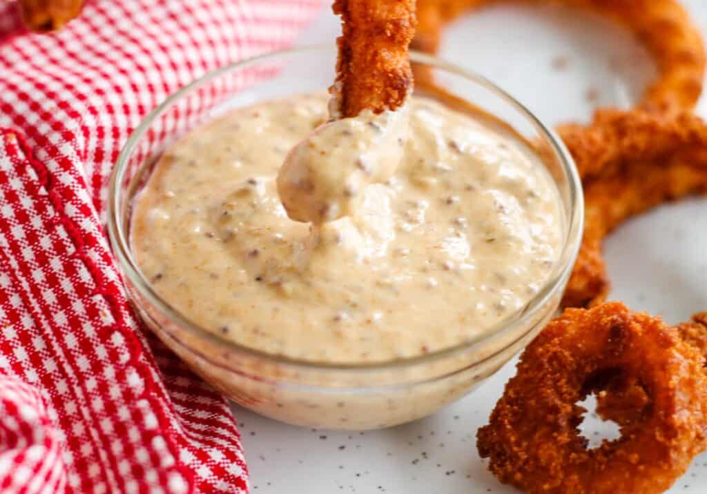 Onion rings with spicy dip in a bowl.