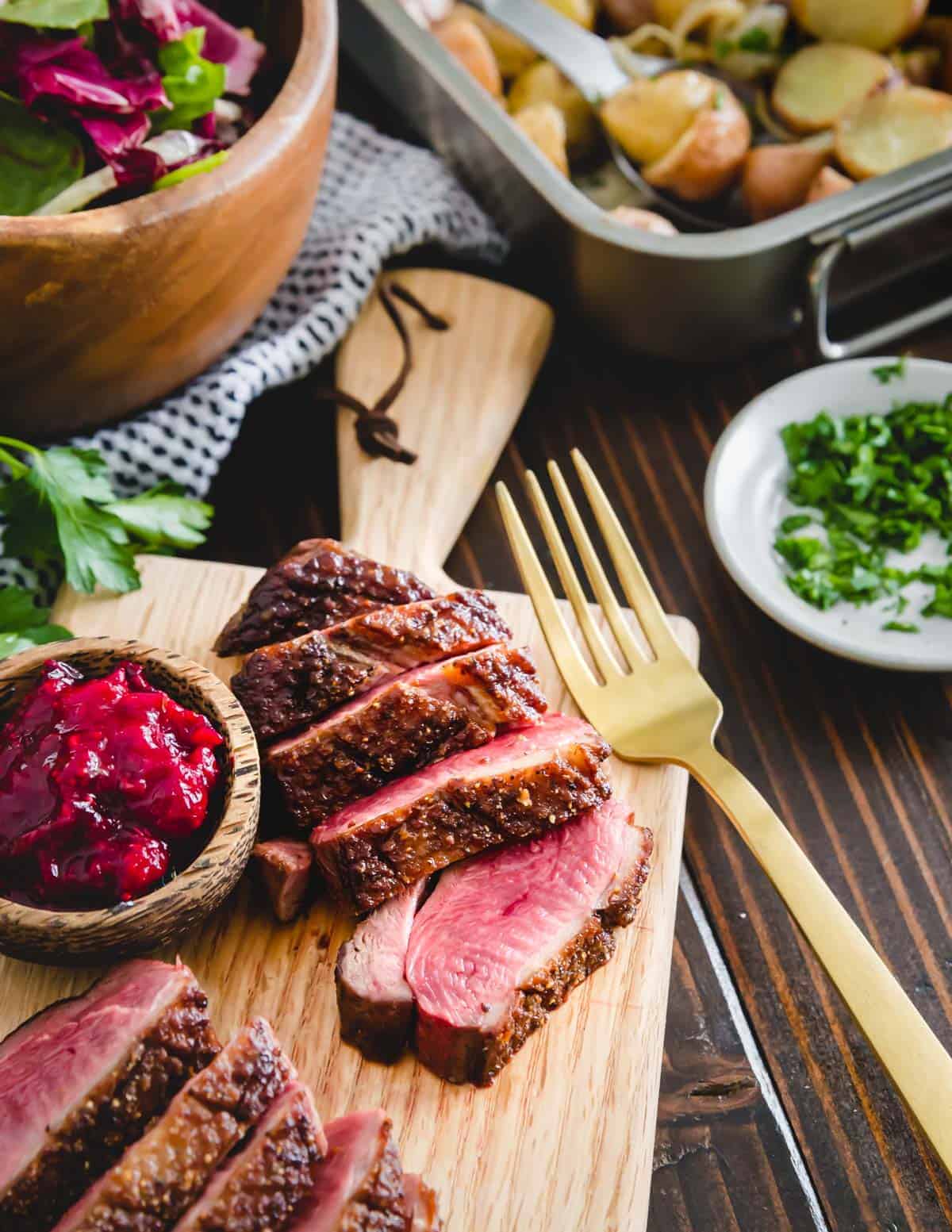 Pan seared duck sliced on a cutting board with cranberry sauce in a small bowl to the side.