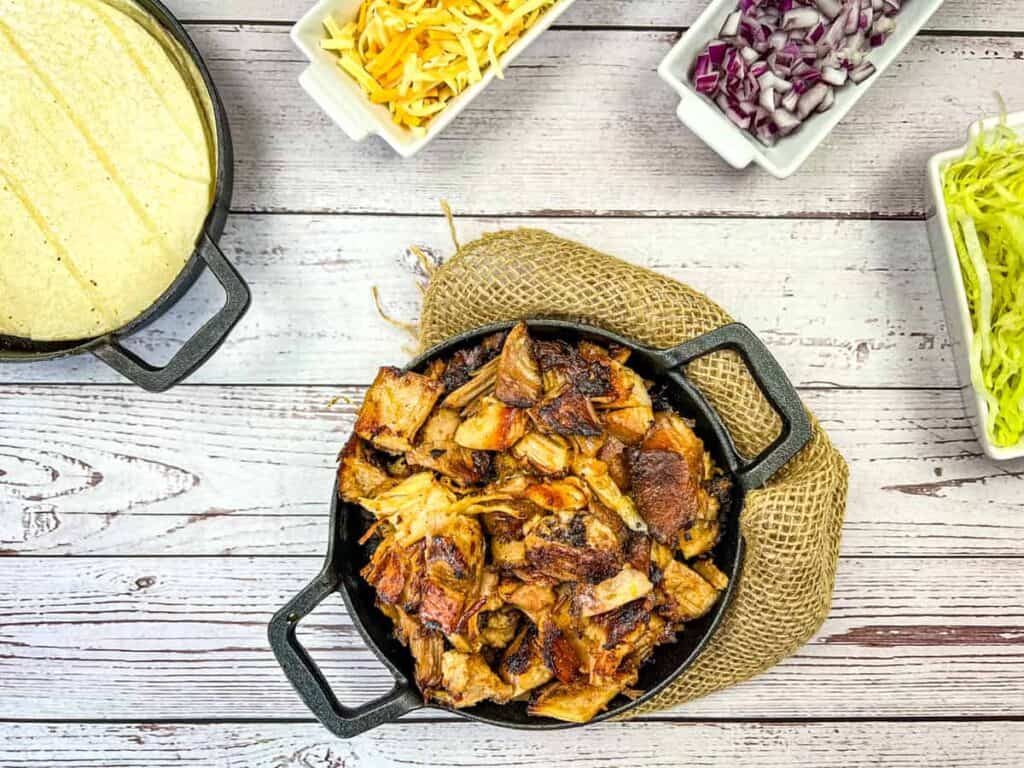 Dutch oven carnitas in a round black dish on a wooden table.