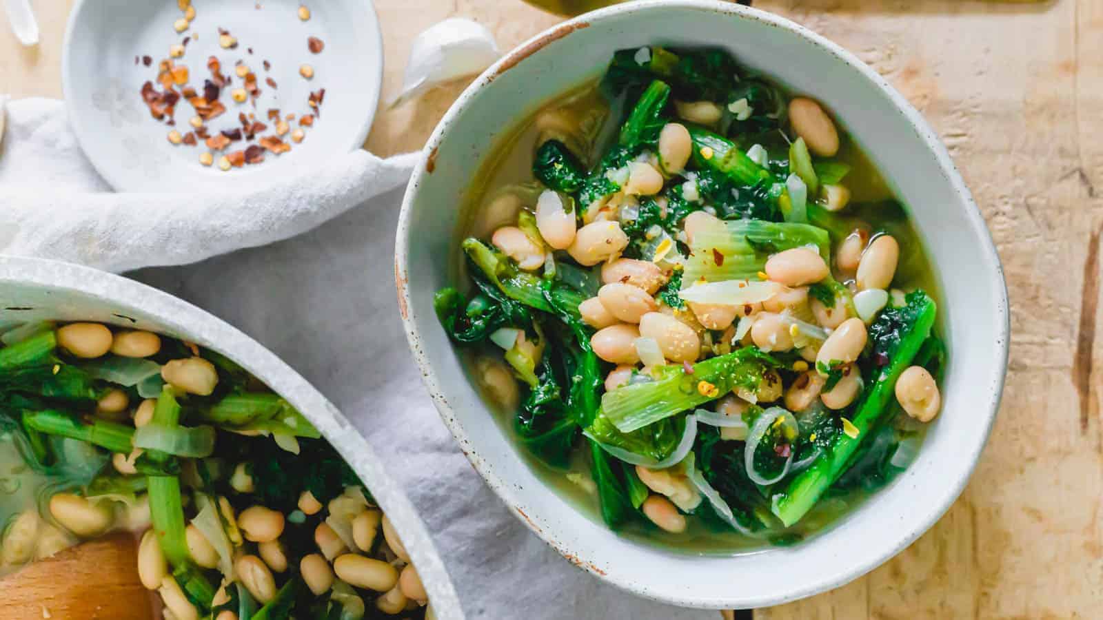 Escarole and beans in a white bowl with red pepper flakes on the side.