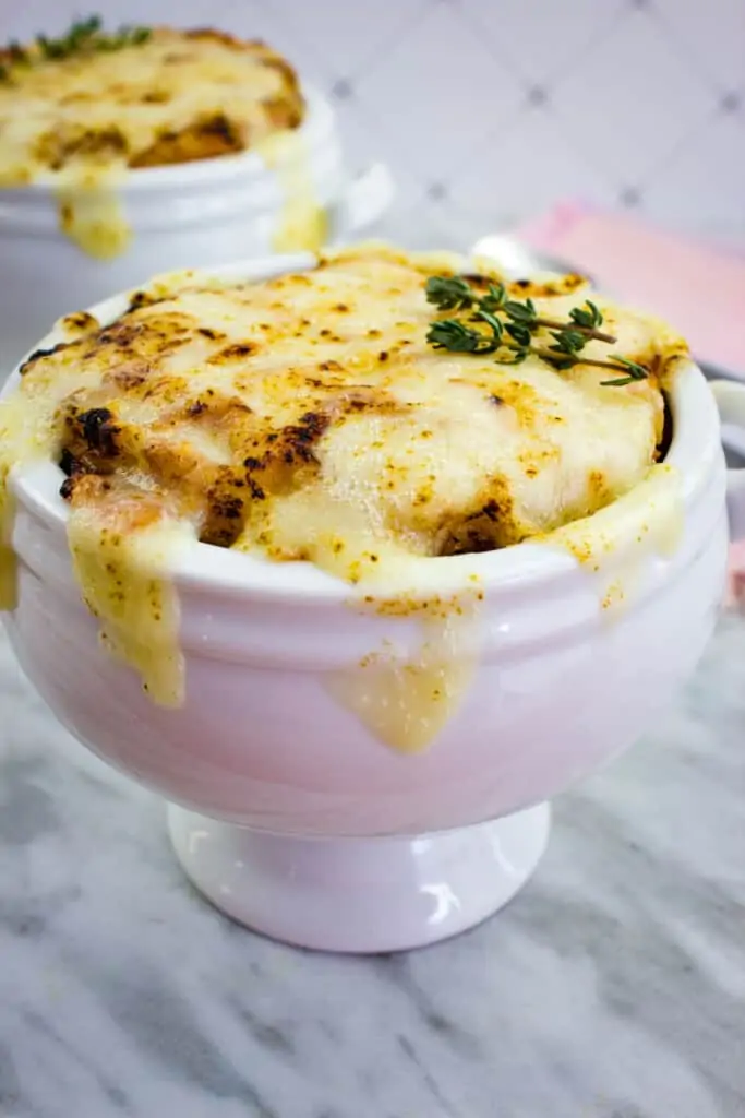 Low-Carb French Onion Soup in a tall white bowl on a marble counter.