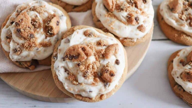 Frosted chocolate chip cookie cookies on a wooden cutting board.