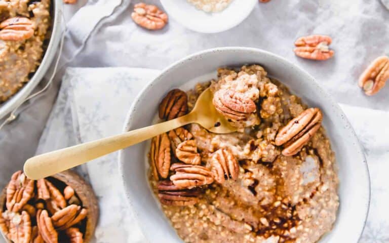 A bowl of oatmeal with pecans and a spoon.