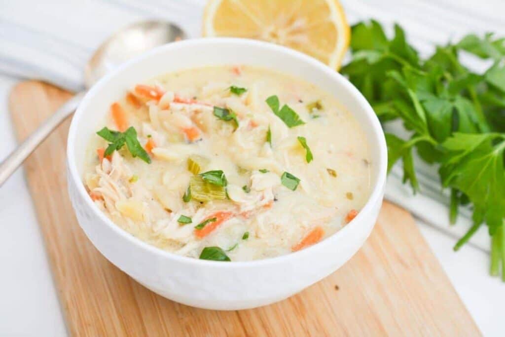 Chicken lemon soup in a white bowl on a cutting board.