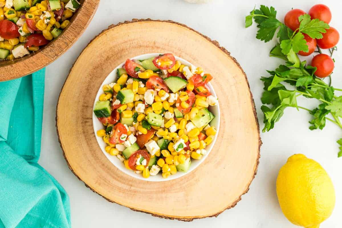 Corn salad mixed together in a white bowl. on top of a decorative wooden platter.