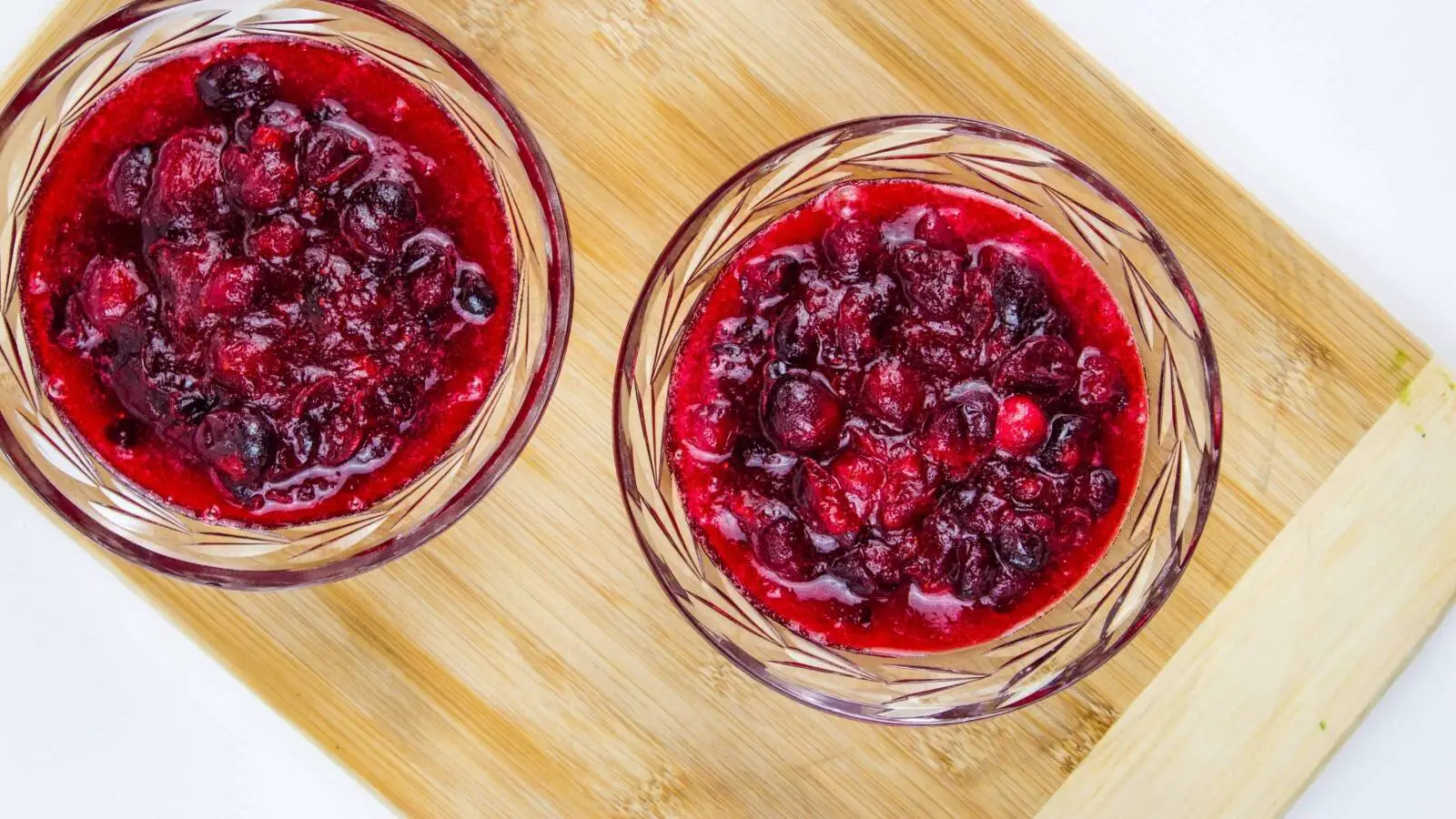 Two bowls of cranberry sauce on a wooden cutting board.