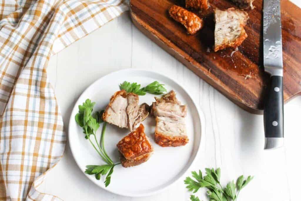 Pork belly bites on a plate with parsley and a knife.