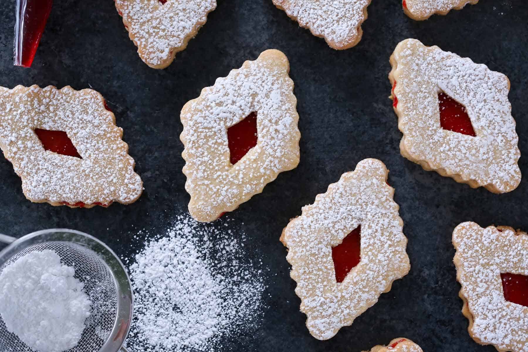 raspberry linzer cookies in diamond shapes on grey surface.