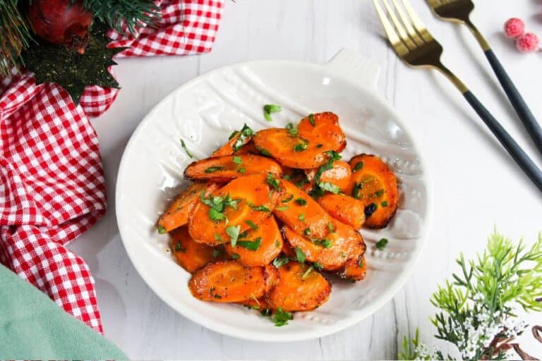 Roasted carrots in a white bowl next to a checkered tablecloth.