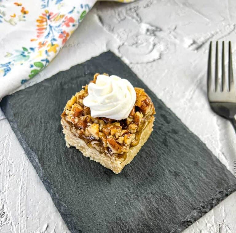 A slice of pecan pie bar with whipped cream on a slate plate.