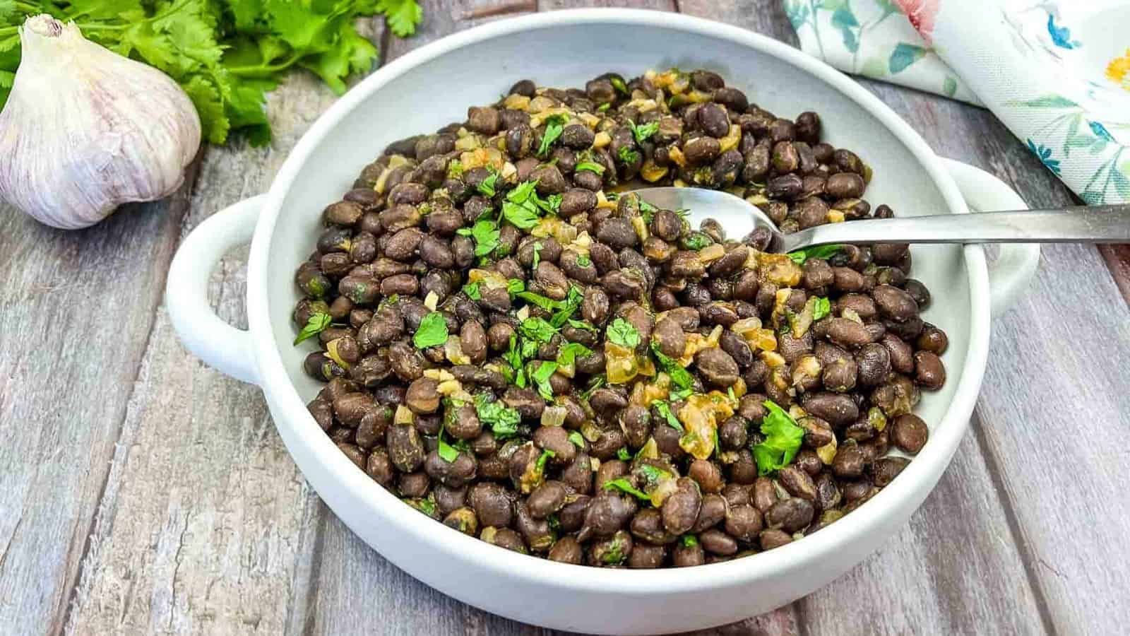 Mexican black beans in a white bowl with parsley and garlic.