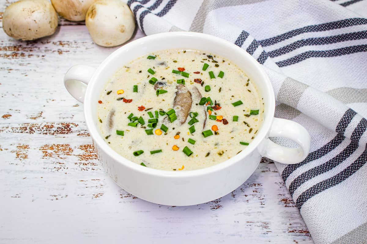 A white bowl of soup with mushrooms and chives that tastes better.