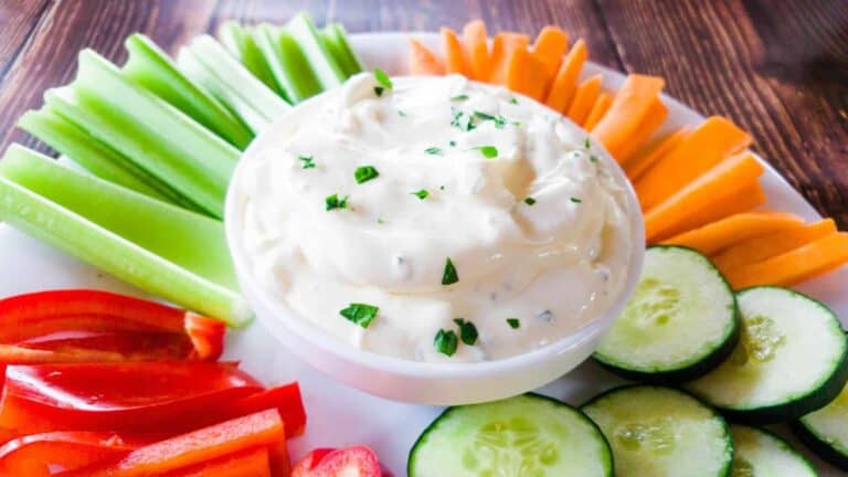 A plate of onion dip with carrots, celery and cucumbers.