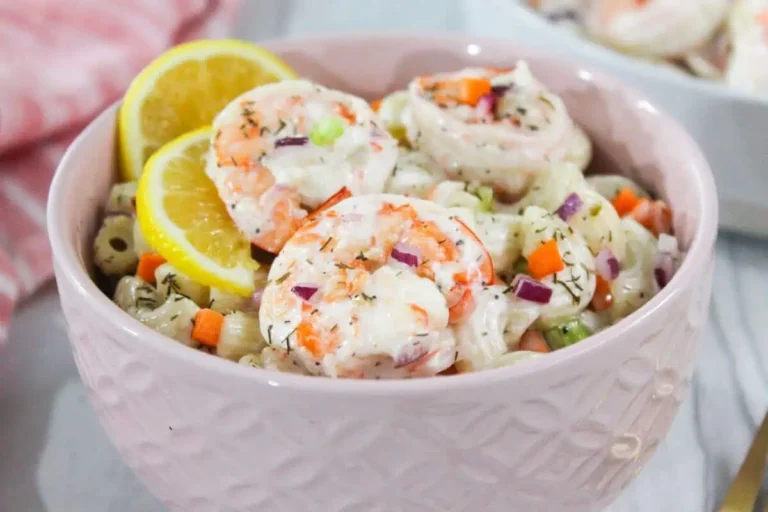 Shrimp salad in a pink bowl with lemon wedges.