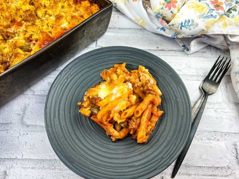 A dinner dish of pasta with meat and cheese on a plate next to a fork.