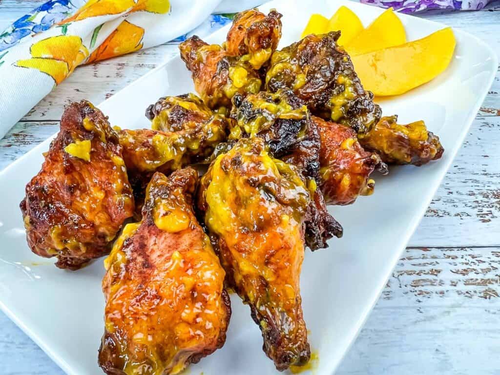 Easy recipes to master in one go - Chicken wings on a white plate with a slice of mango.