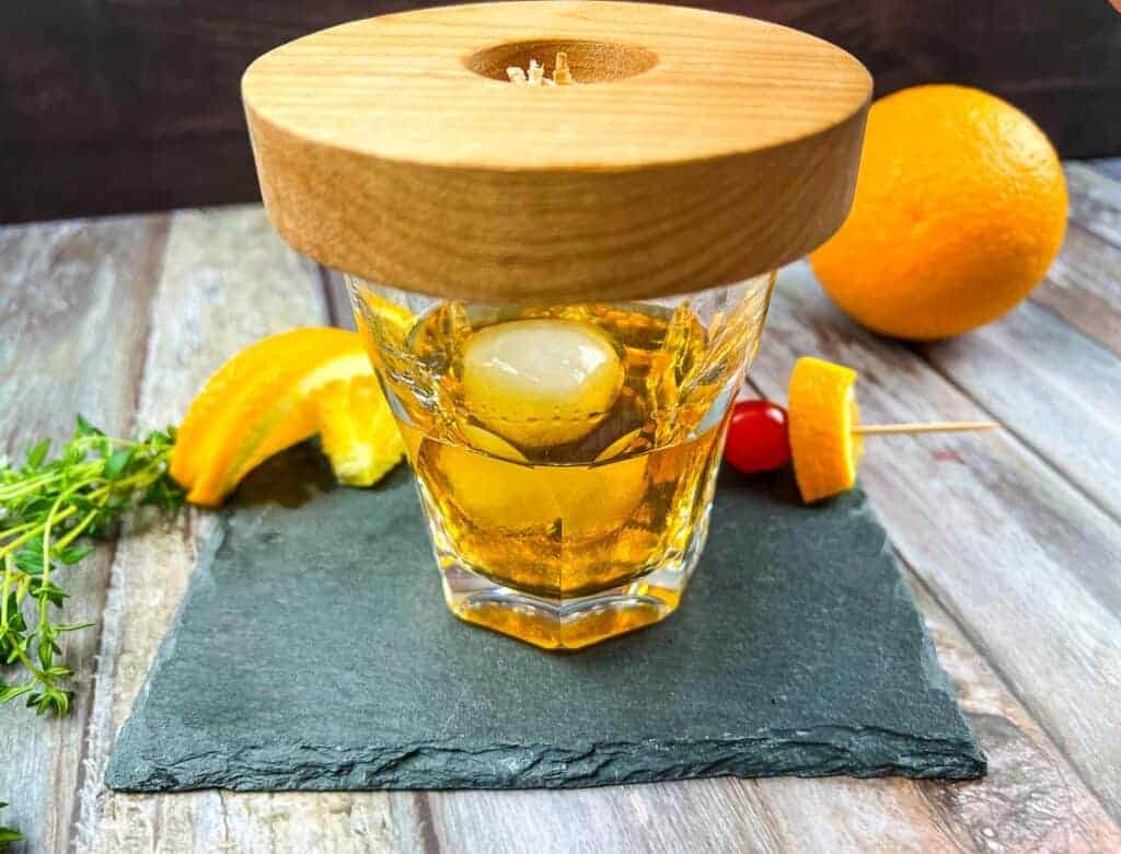 A glass of whiskey with oranges and a wooden stick.