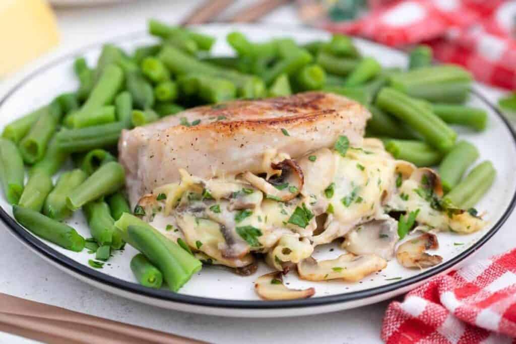 A plate of chicken breast with mushrooms and green beans.