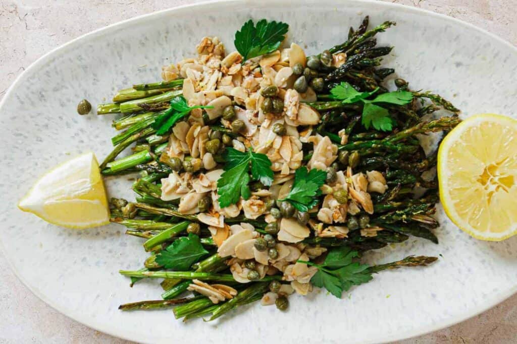 A plate with asparagus, nuts and lemon wedges.