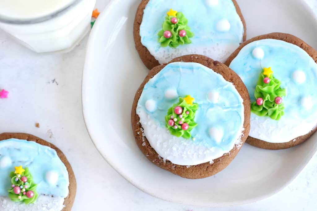 A plate of christmas cookies with icing and a glass of milk.