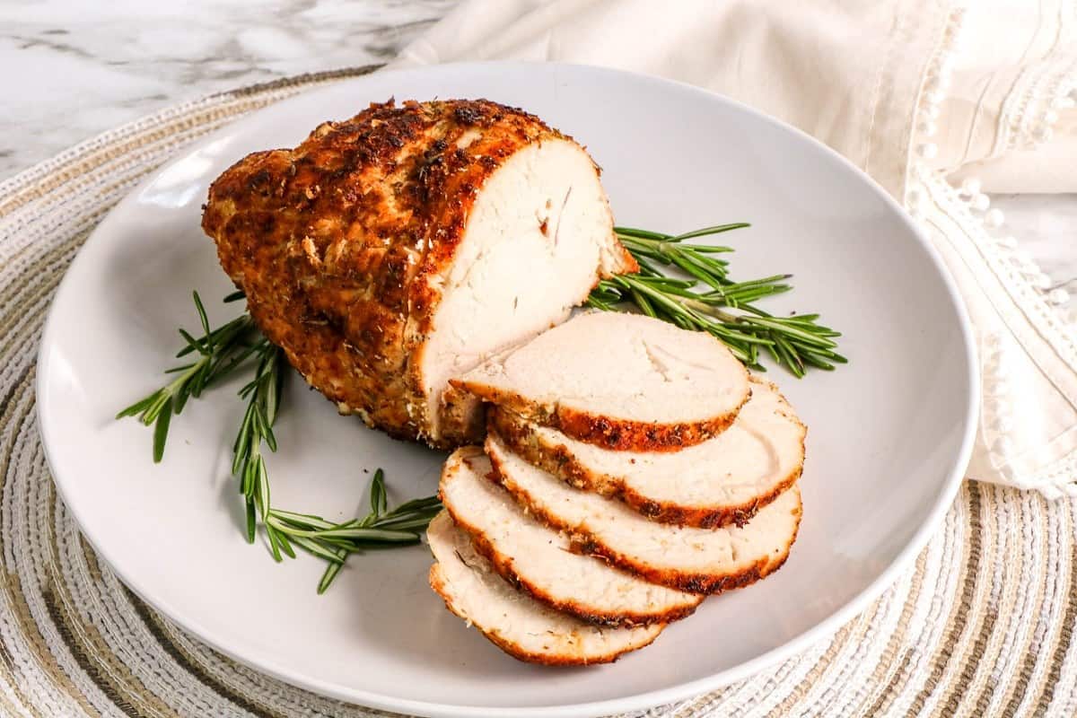 Sliced roasted turkey on a white plate with rosemary sprigs.