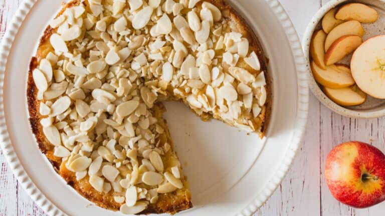 A slice of apple cake with almonds on a plate.