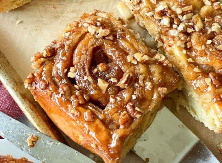 Apple Cinnamon rolls topped with pecans on a cutting board.