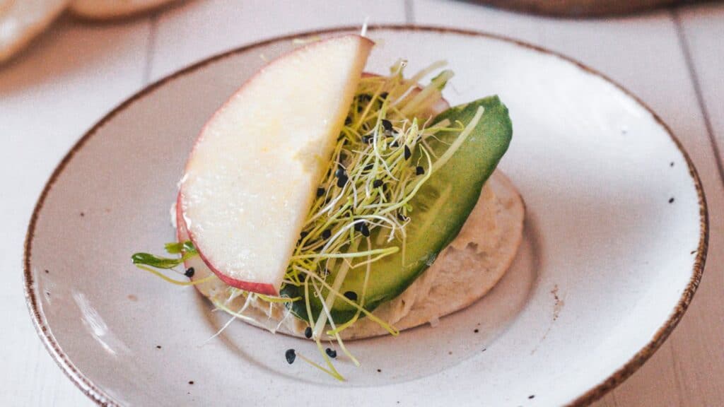 A sandwich with an apple and sprouts on a plate.