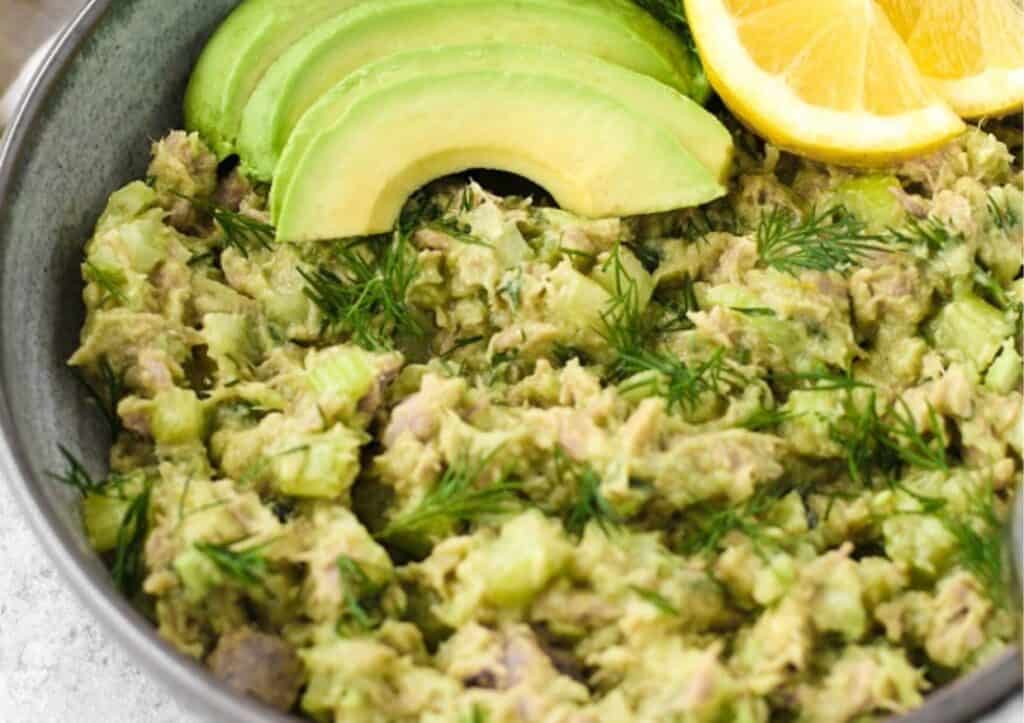 Avocado tuna salad in a bowl with avocado and lemon slices.