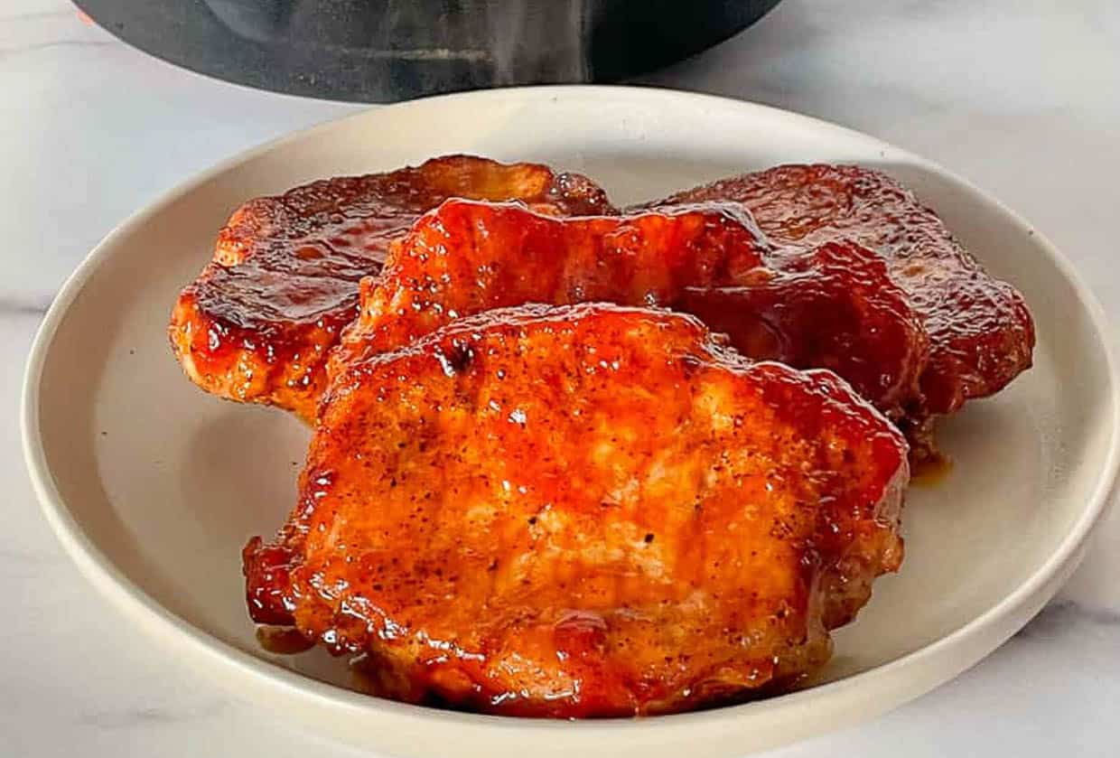 Pork chops in a cast iron skillet with bbq sauce on the chops.