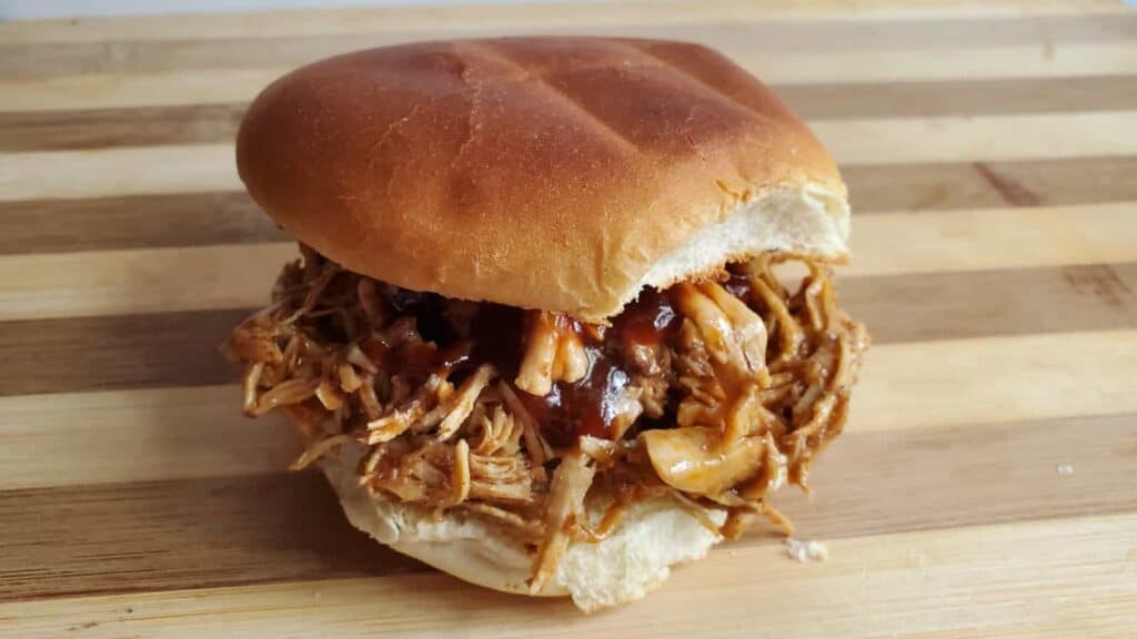 Image shows a shredded bbq chicken sandwich on a wooden board.