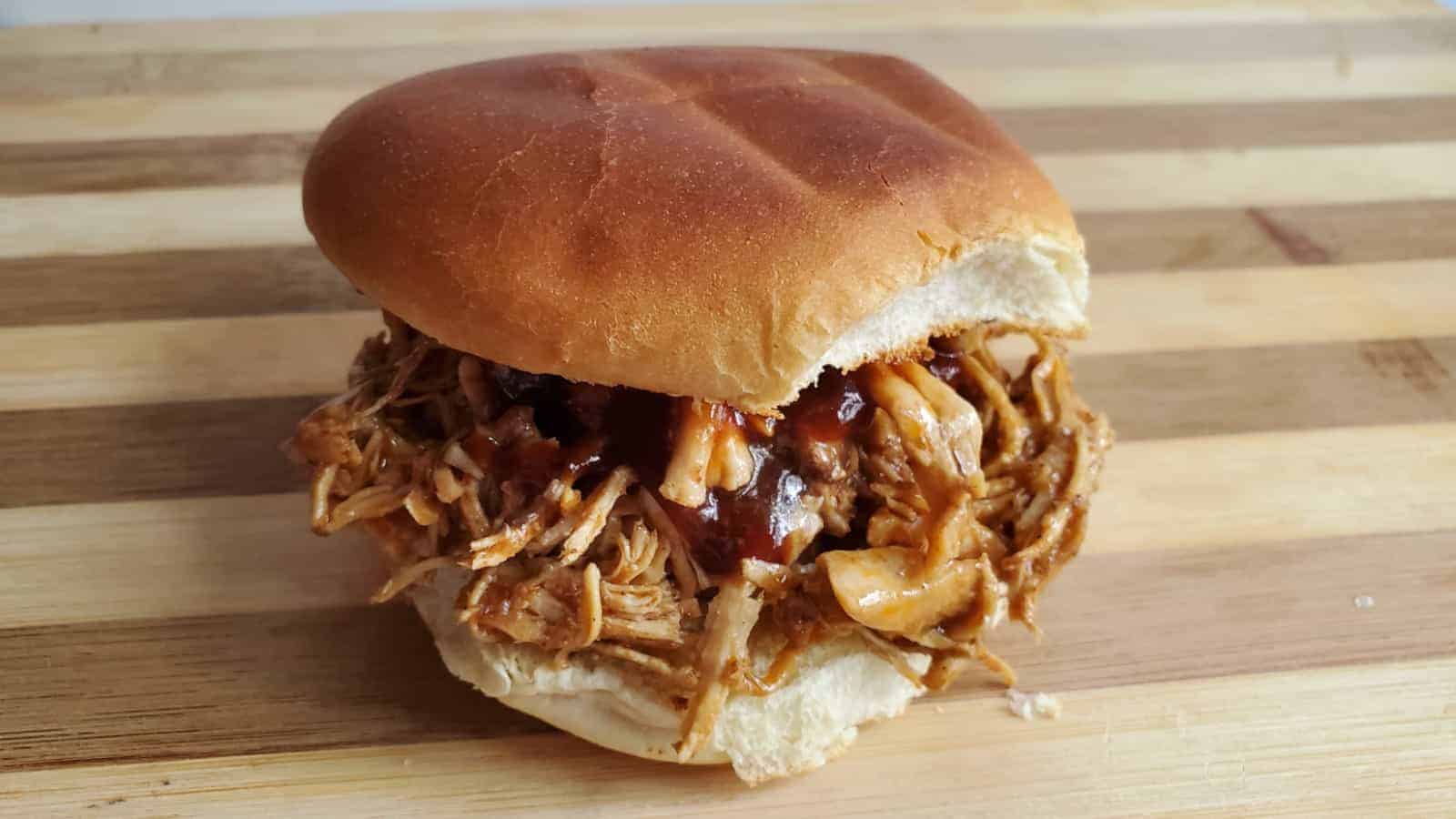 Image shows a BBQ shredded chicken sandwich on a wooden board.
