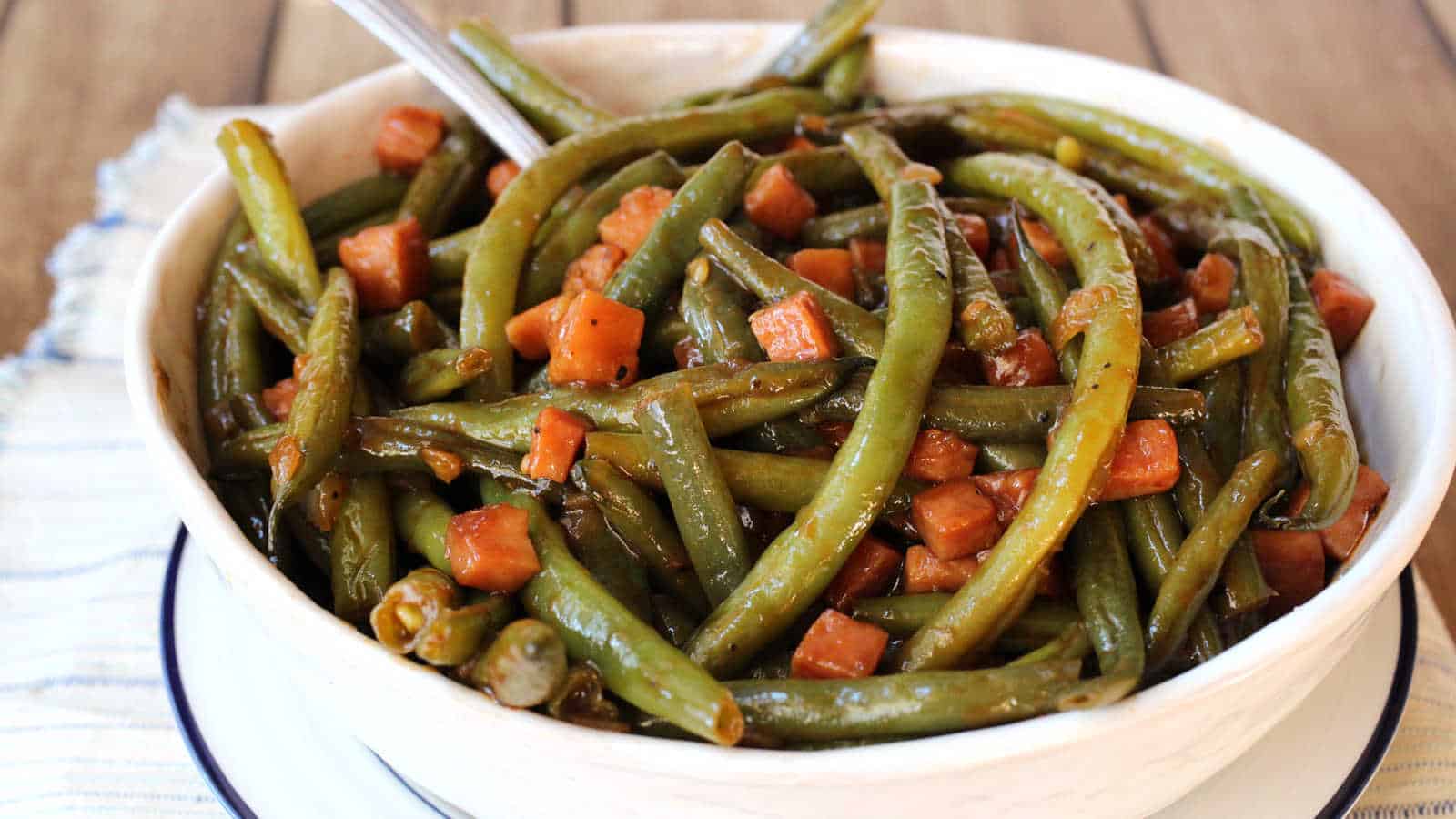 A white bowl with barbecued green beans and chuncks of ham.