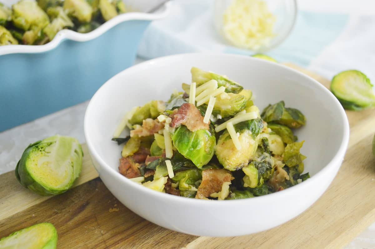 Brussels sprouts and bacon in a bowl on a cutting board.