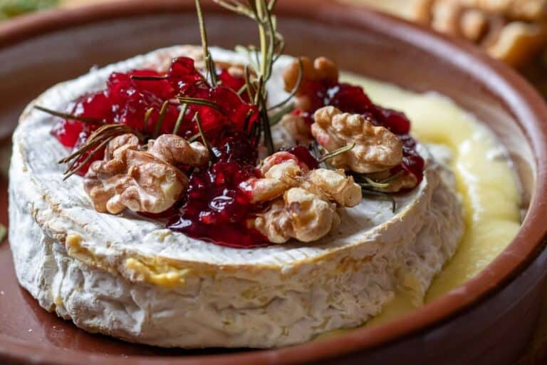A cheese with cranberries and jam on a plate.