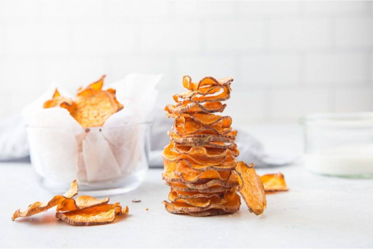 A stack of sweet potato chips next to a glass of milk.