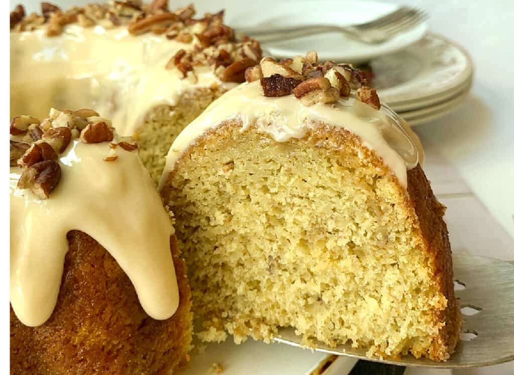 A bundt cake with icing and pecans on a plate.