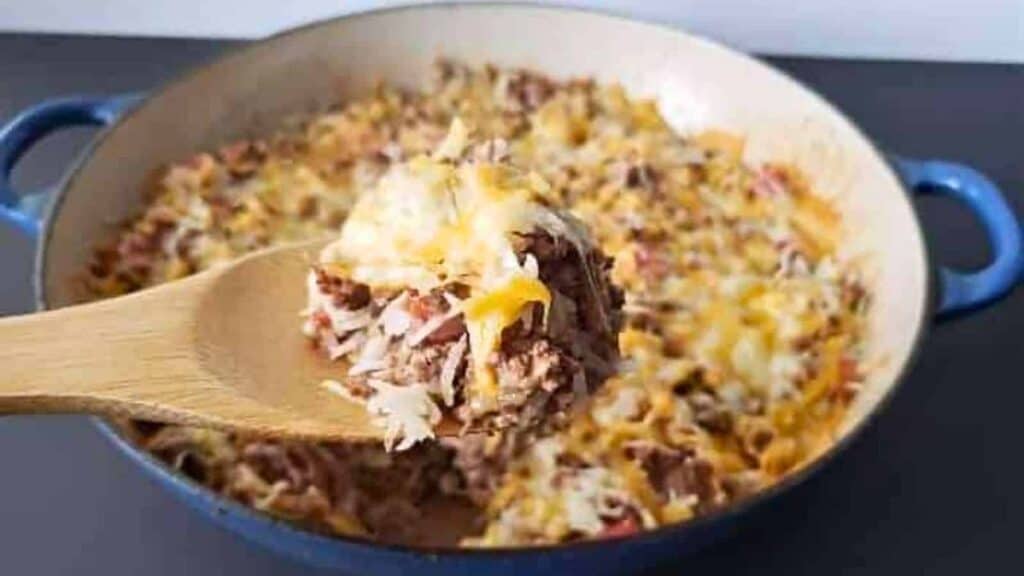 A wooden spoon is being lifted out of a casserole dish.