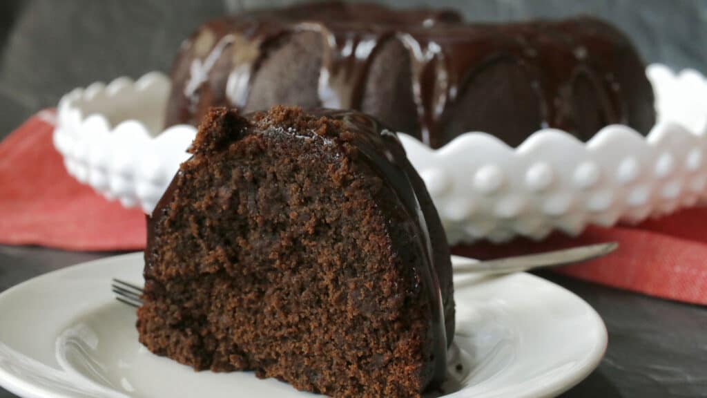 A chocolate bundt cake on a plate with a slice taken out.