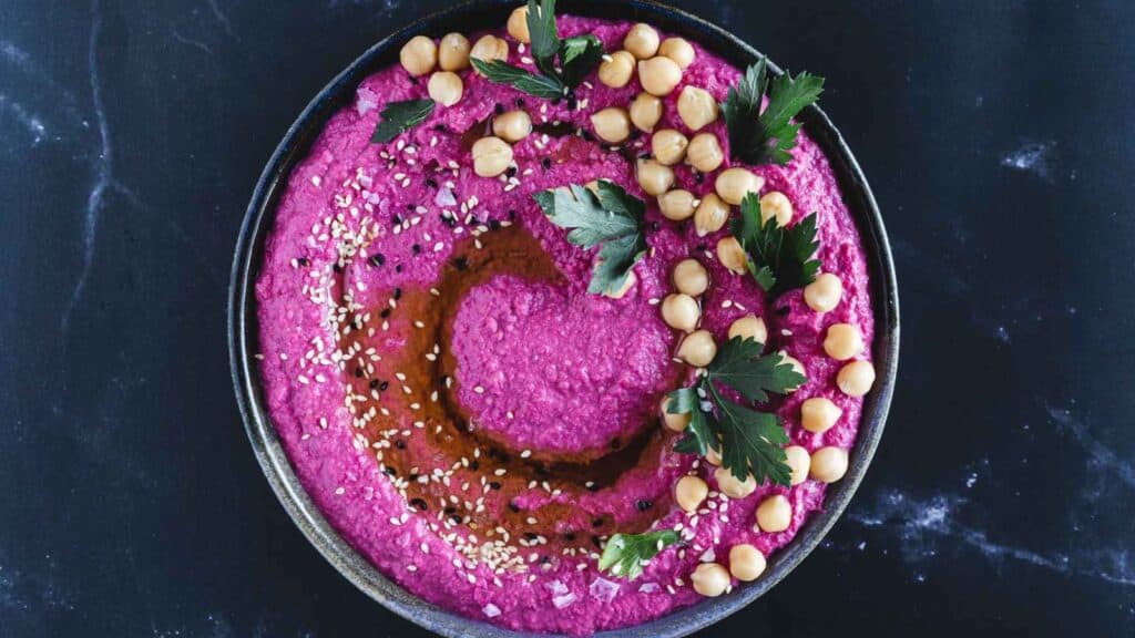 A bowl of pink hummus with chickpeas and parsley, perfect for holiday appetizers.