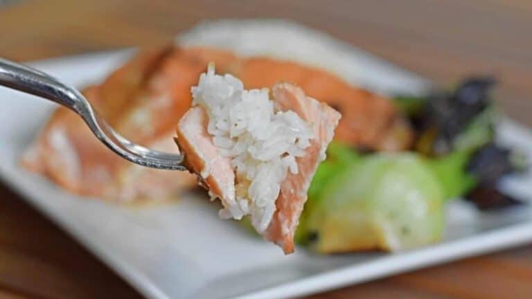 Image shows a Bite of miso glazed salmon with rice on a fork with the rest of the plate in the background.