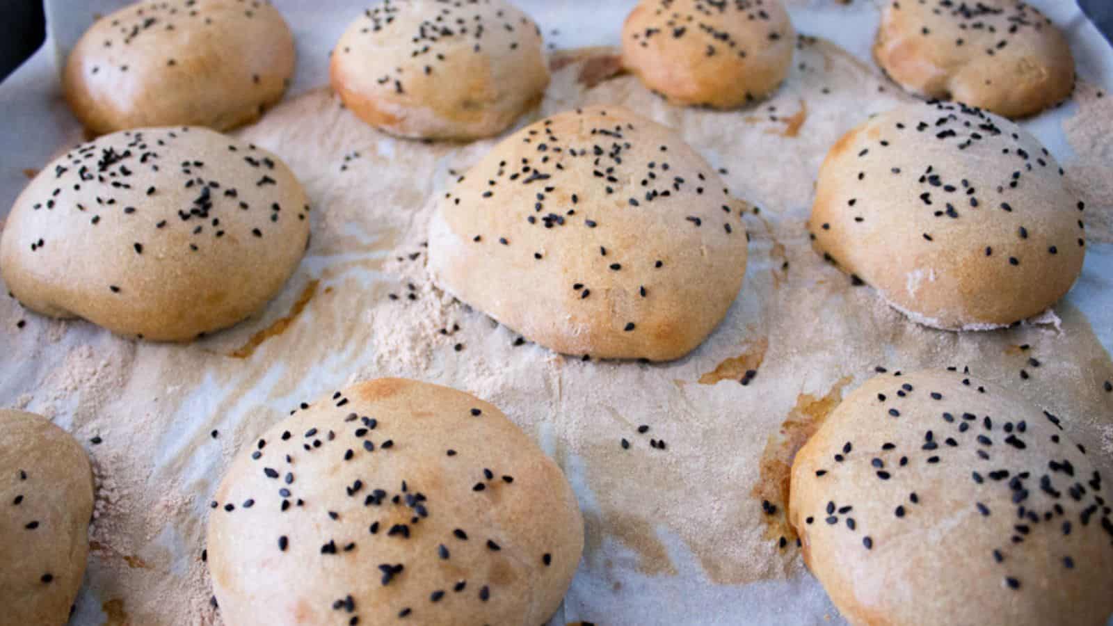 Sesame buns with sesame seeds on a wooden cutting board.