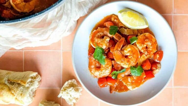 A plate of shrimp with tomatoes and bread on a tiled floor.