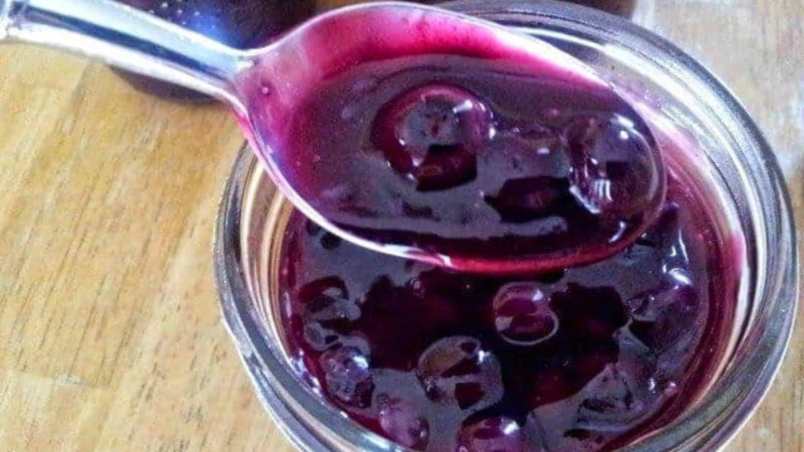 Overhead shot of a spoon containing blueberry syrup being held over a jar with more syrup.