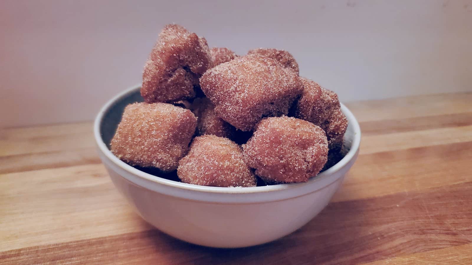 Image shows a blue Bowl of pumpkin donuts on a wooden board.