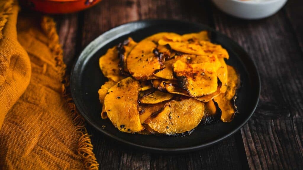 A plate of roasted sweet potatoes on a wooden table.