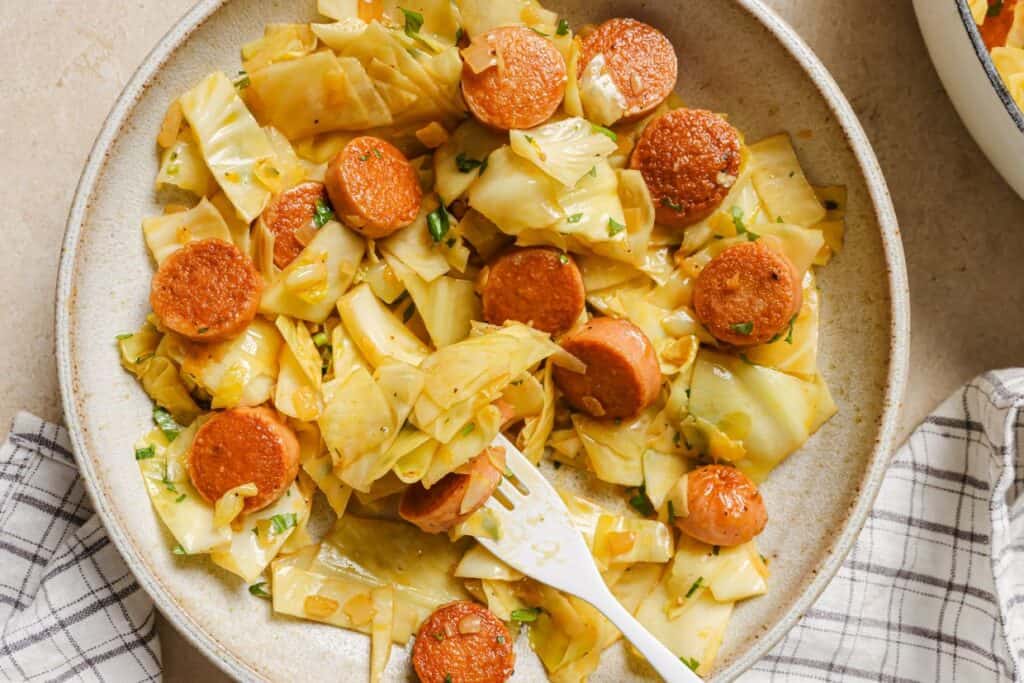 A plate of cabbage and sausages with a fork.