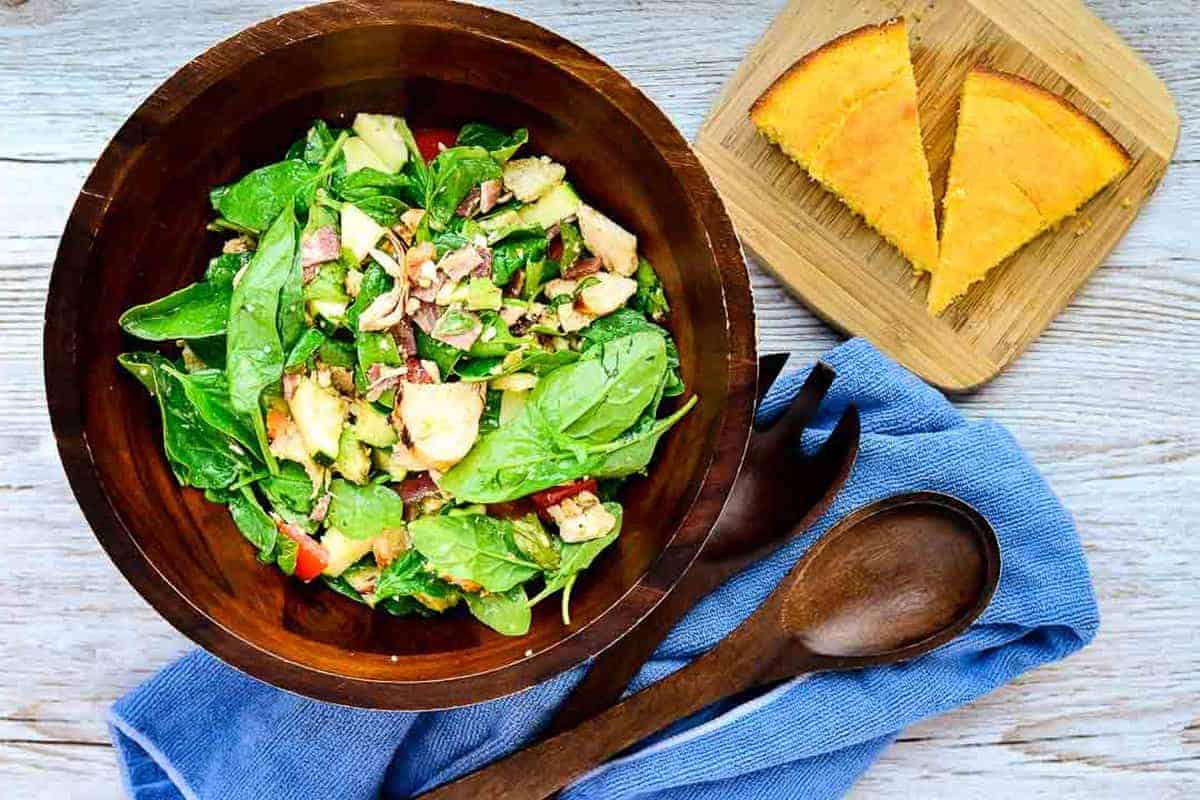 A bowl of spinach salad with apples and walnuts.