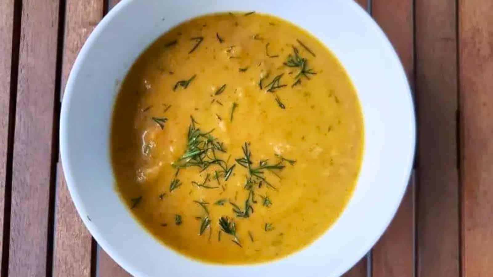 Image shows A bowl of carrot chicken soup on a wooden table.