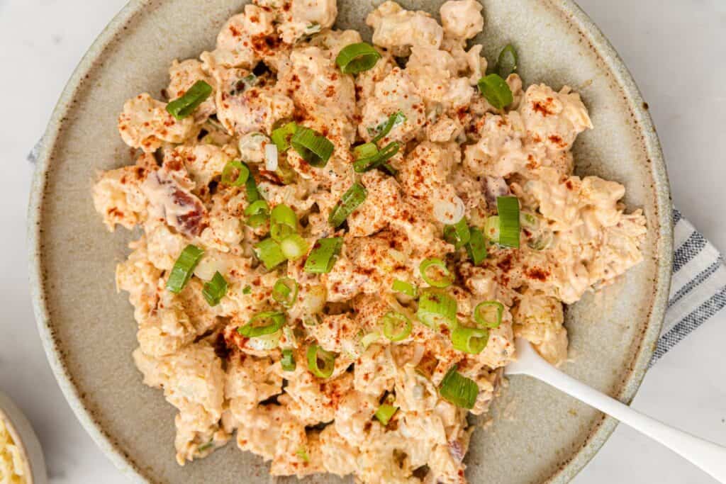 A bowl of cauliflower potato salad on a table with a spoon.